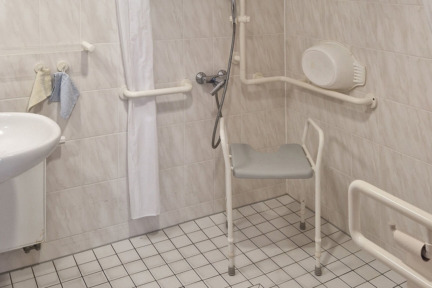 Barrierefreies Badezimmer mit Ebenerdiger Dusche, Duschhocker und Haltegriffe an den Wänden.
