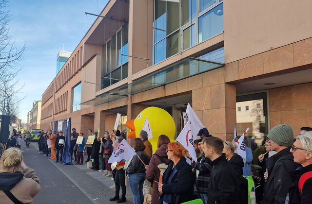 Viele Menschen mit Schildern und auch AWO Fahnen die hochgehalten werden. Auf einem Gehweg vor einem langen großen Gebäude mit vielen Fenstern.