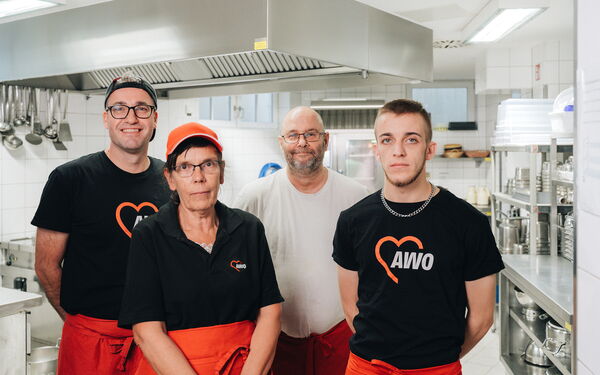 Teamfoto. In einer Großküche. Drei Männer und eine Frau stehen und lächeln in die Kamera.
