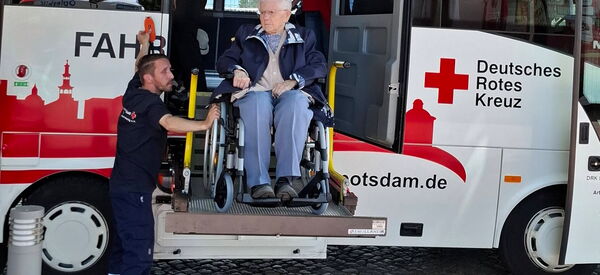 Reisebus vom Deutschen Roten Kreuz mit Hebebühne. Ein älterer Herr im Rollstuhl wird vom DRK Mitarbeiten aus Bus befördert.
