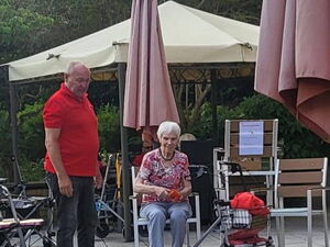 Seniorin sitzt  auf Terrasse. Dosen Pyrapide steht vor ihr auf dem Boden. Sie wirft danach.