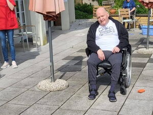 Senior im Rollstuhl auf der sonnigen Terrasse. Vor ihm steht der Rest einer Büchsen-Pyramide.
