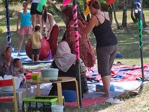 Wiese, Bäume, ein Pavillon, darunter sitzen Menschen auf ausgebreiteten Decken.