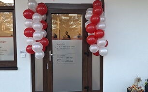 Glastür mit roten und weißen Luftballons rechts und links, über der Tür ein Schild der Sozialstation Bad Belzig mit dem AWO-Logo