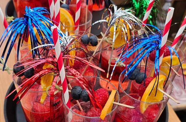Party Gläser mit Erdbeerbowle, Strohhalmen und Deko auf einem runden Tablett.