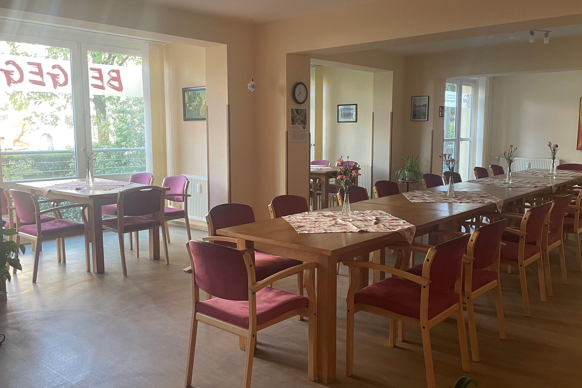 im Vordergrund steht eine lange Tischtafel mit Stühlen. Im Hintergrund stehen kleinere Sitzgruppen in den vorhandenen Fensternischen.