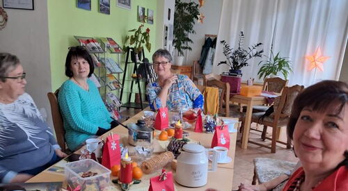 Gedeckter Kaffeetisch mit kleinen Weihnachtstüten und Süßigkeiten. Vier Frauen sitzen an dem Tisch.