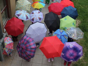 Personen mit vielen bunten Regenschirmen auf einem Weg neben einem Gebäude.
