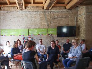 Raum. Menschen sitzen in Kreisen. An der Wand sind Schilder mit Forderungen zum Thema Wohnen.