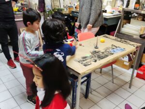 3 Kinder asiatischen Aussehens, schwarze Haare. Zwei der Kinder stehen an einem kleinen Tisch.