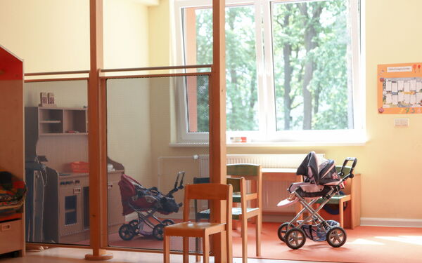 Ein Raum mit großen Fenstern. Zwei Kinderwägen stehen auf einem Teppich.