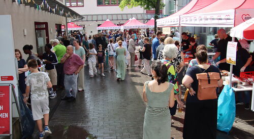 Viele Menschen auf dem Gelände. Essensstand mit roten AWO Pavillons überdacht. Gebäude rahmen das Gelände ein.