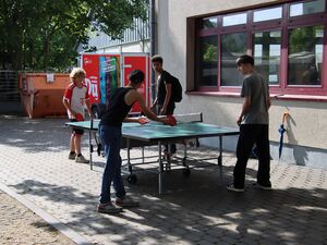 Draußen, Sonne scheint. 4 Jugendliche an einer Tischtennisplatte. Es sind 4 Jungs.