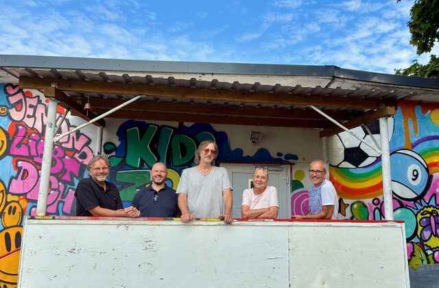 Gruppenbild. 5 Menschen, darunter eine Frau vor einer mit Graffiti besprühten Wand.