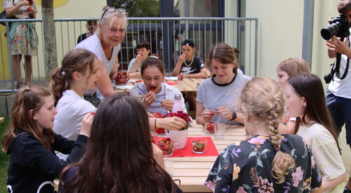Draußen. Kinder sitzen um einen Tisch und essen Erdbeeren.