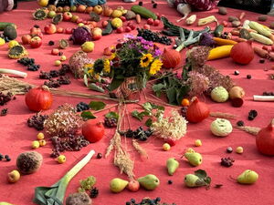 Großer runder roter Teppich darauf Blumen, Obst und Gemüse kreisförmig. Kinder und Erwachsene am Rand.