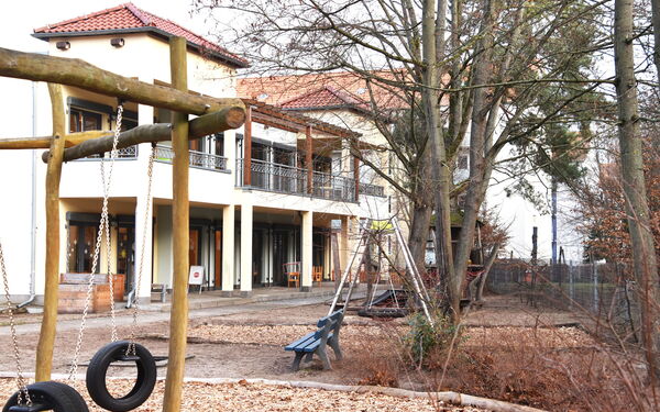 Draußen, Kita Gebäude und ein Teil des Spielplatzes.