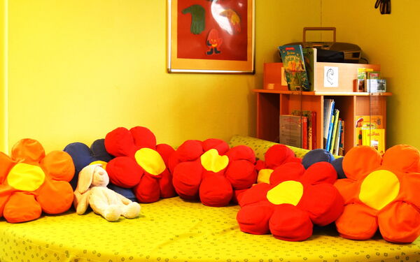 Spielzimmer, großes gelbes Sofa mit großes Kissen in Blumen-Blüten-Form. Gelbe Wände hat der Raum.