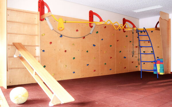 Sportraum. Mit Kletterwand, Sprossenwand, ein Ball liegt auf dem Fußboden, Eine Bank ist an die Sprossenwand gelehnt.