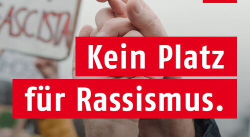 AWO Logo oben in der Ecke. Text: Kein Platz für Rassismus. | Demokratie macht Zukunft. Szene einer Demonstration verschwommen im Hintergrund. Zwei erhobene Hände die sich festhalten.