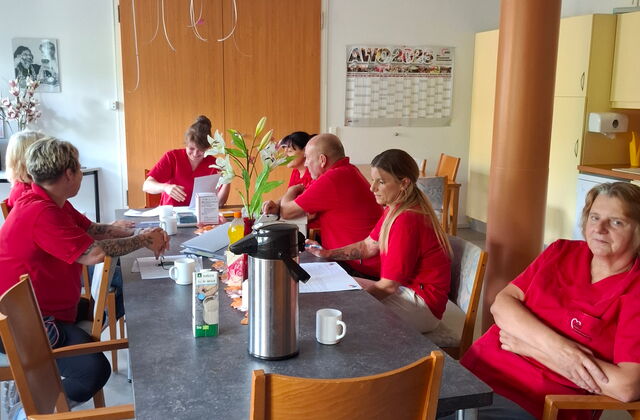 Team in roten AWO Shirts sitzt an einem Tisch mit Unterlagen und Kaffee. Team Sitzung.