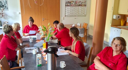 Team in roten AWO Shirts sitzt an einem Tisch mit Unterlagen und Kaffee. Team Sitzung.