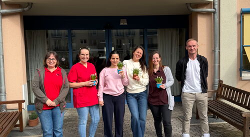 5 Frauen und ein Mann vor dem Eingang eines Seniorenzentrums. Sie jungen Frauen haben kleine Blumentöpfe in der Hand.