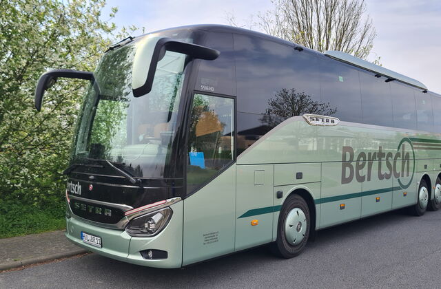 Reisebus auf einem Parkplatz, daneben Bäume und Grünfläche.