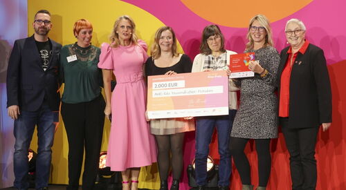 Gruppenbild mit Scheck über 2.000 Euro. Ein Mann und sechs Frauen stehen in einer Reihe, lächeln und 2 der Frauen halten den Preis-Scheck vor sich.