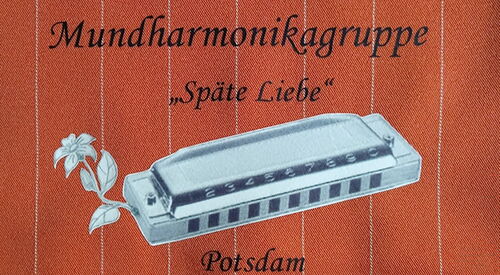 Logo der Mundharmonikagruppe auf einem Stück Stoff aufgestickt. Die Aufschrift neben dem Instrument ist: Mundharmonikagruppe, Späte Liebe, Potsdam.