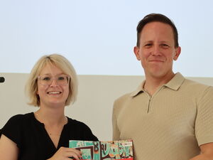 Eine Frau und ein Mann halten lächelnt eine Broschüre der Jugendaktionswoche in die Kamera.
