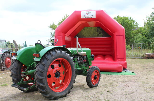 Grüner Traktor vor roter Hüpfburg.