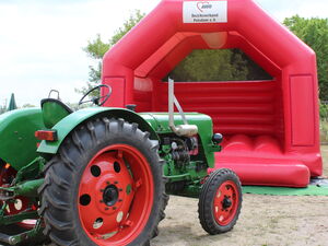 Grüner Traktor vor roter Hüpfburg.