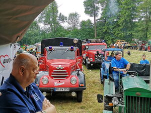 Menschen im Traktoranhänger. Dahinter fahren Traktoren und alte Feuerwehrautos.