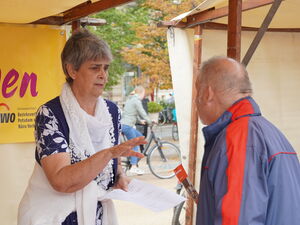 AWO erleben Stand mit gelben Banner. Eine Frau im Gespräch mit einem älteren Mann.