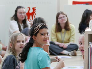 Kinder und Jugendliche sitzen auf dem Boden im Plenarsaal. Mädchen dreht sich um und lächelt in die Kamera.