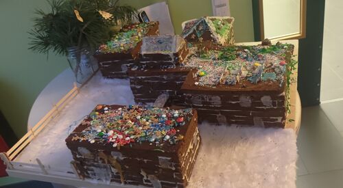 Lebkuchen-Kita-Komplex mit weißem Zeug das Schnee darstellen soll. Die Lebkuchen-Gebäude sind bunt mit Süßigkeiten dekoriert. Sie steht auf einem runden Tisch.