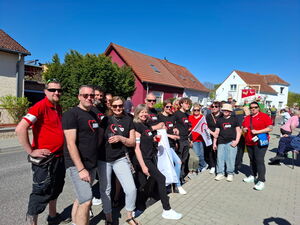 AWO Mitarbeitende auf der Straße und Gehweg inn dunklen und roten AWO T-Shirts mit Fahnen.