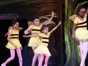 Vier Mädchen in Bienen-Kostümen und rosa Strumpfhosen tanzen auf der Bühne.