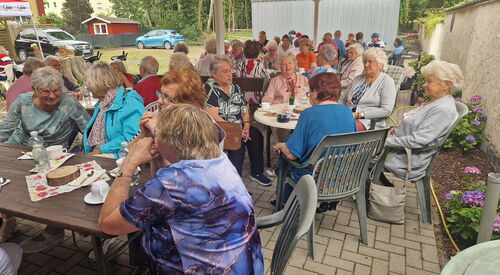 Viele ältere Menschen auf Gartenstühlen und Kaffeetafeln.