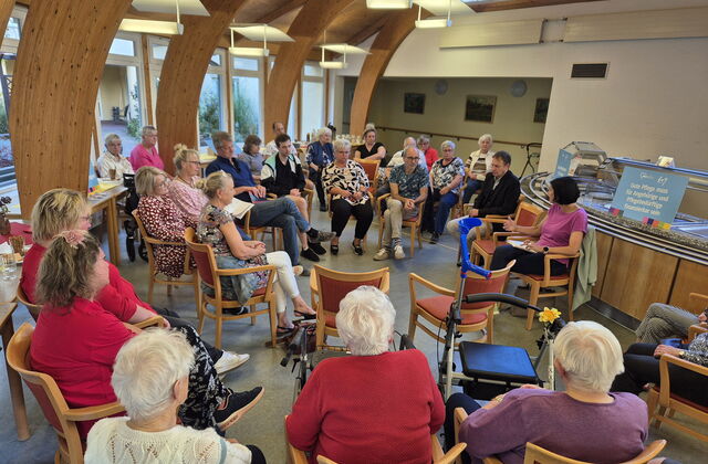 Großer Raum, Kantine, viele Menschen sitzen kreisförmig. Diskussionsrunde.