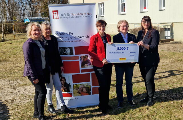 Draußen, Sonne scheint. Mittig ein Roll-Up von „Hilfe für Familien in Not“. Links davon zwei lächelnde Frauen. Rechts davon drei Frauen halten Scheck in die Kamera.