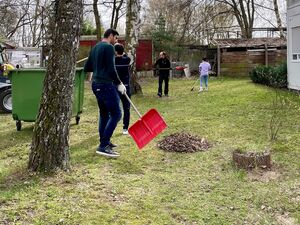 Draußen. Menschen beim Frühjahrsputz, Bäume, Sträucher, Laubhaufen. Mann mit Schaufel.