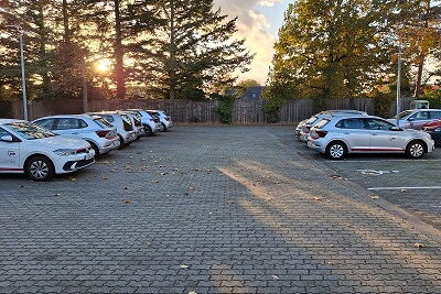 gepflasterte große Parkfläche, links vom Bild stehen 6 Autos der AWO hintereinander, rechts vom Bild 3 Autos der AWO und einem barrierefreiem Parkplatz