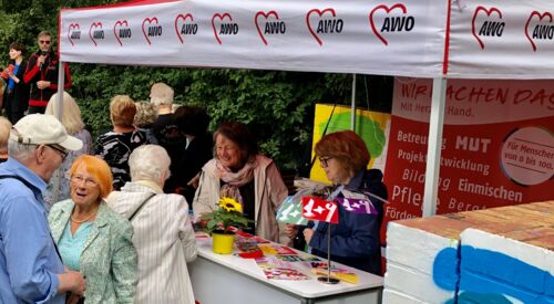 Stand der AWO Potsdam, roter Pavillon. Zwei Frauen stehen am Stand der AWO und beraten. Einige ältere Menschren stehen drum rum und unterhalten sich.