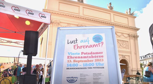 Nahaufnahme vom Aufsteller Text: Lust auf Ehrenamt? Vierte Potsdamer Ehrenamtsbörse 13. September 2023, 14 - 18 Uhr. Im Hintergrund ist das Brandenburger Tor in Potsdam.