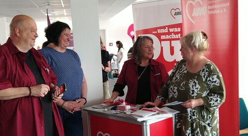 Mitarbeitende und Ehrenamtliche der AWO stehen um einen Messetisch. Im Hintergrund sind Banner des AWO Bezirksverbandes und der Ehrenamtsagentur zu sehen.