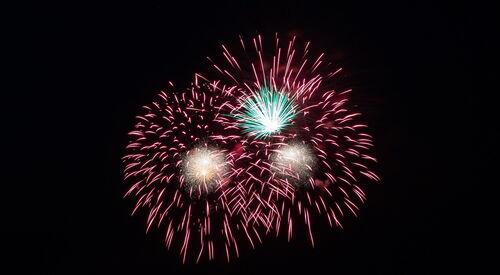 Ein Feuerwerk. Drei Feuerwerkskörper die bunt explodieren. Schwarzer Hintergrund.