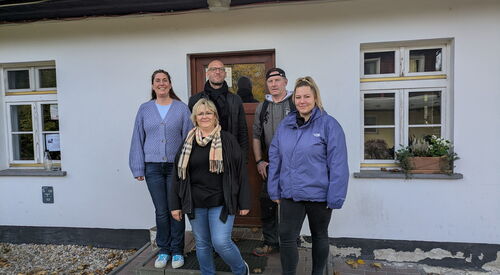 2 Männer, drei Frauen stehen auf den Eingangsstufen zu einem weißen Haus mit brauner Tür. Sie schauen alle in die Kamera. ganz links: Julia Doppler
