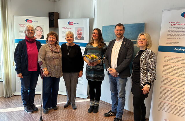 Gruppenbild vor Ausstellungstafeln. 5 Frauen und ein Mann. Die Frau in der Mitte hat einen Blumenstrauß in den Händen.